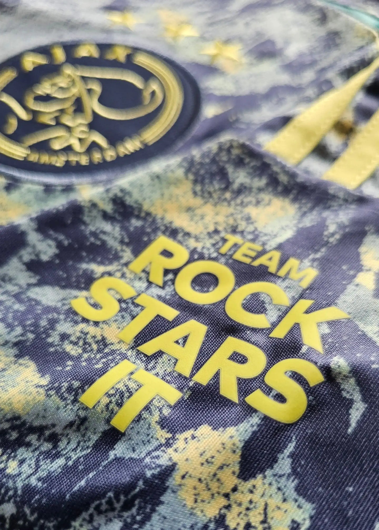 Close-up of Ajax crest with three stars and text "TEAM ROCK STARS IT" in yellow.