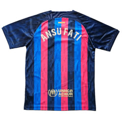 Back view showing name ANSU FATI and UNHCR ACNUR logo on red and blue striped shirt.