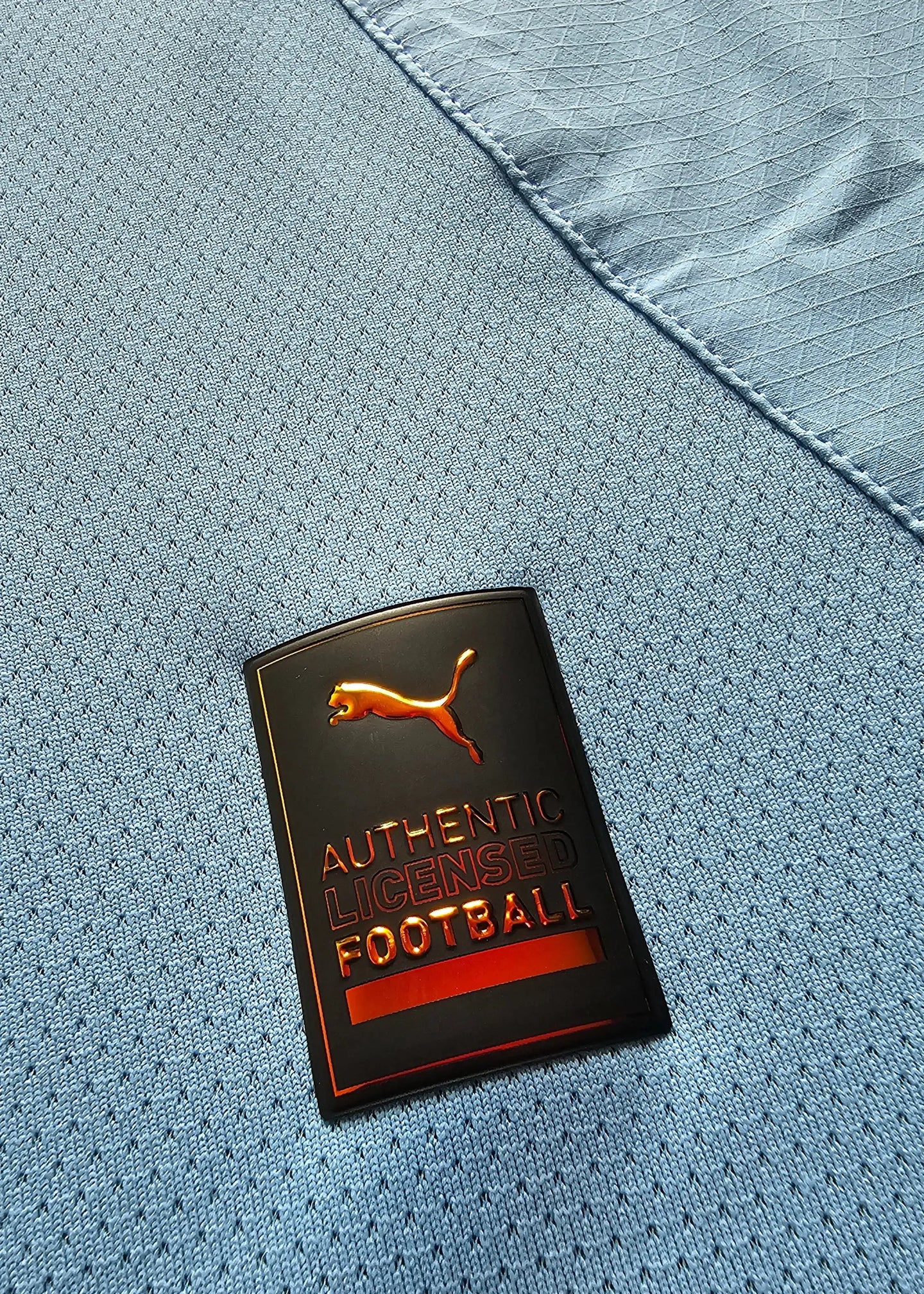 Close-up of the Puma tag showing 'AUTHENTIC LICENSED FOOTBALL' on blue fabric.