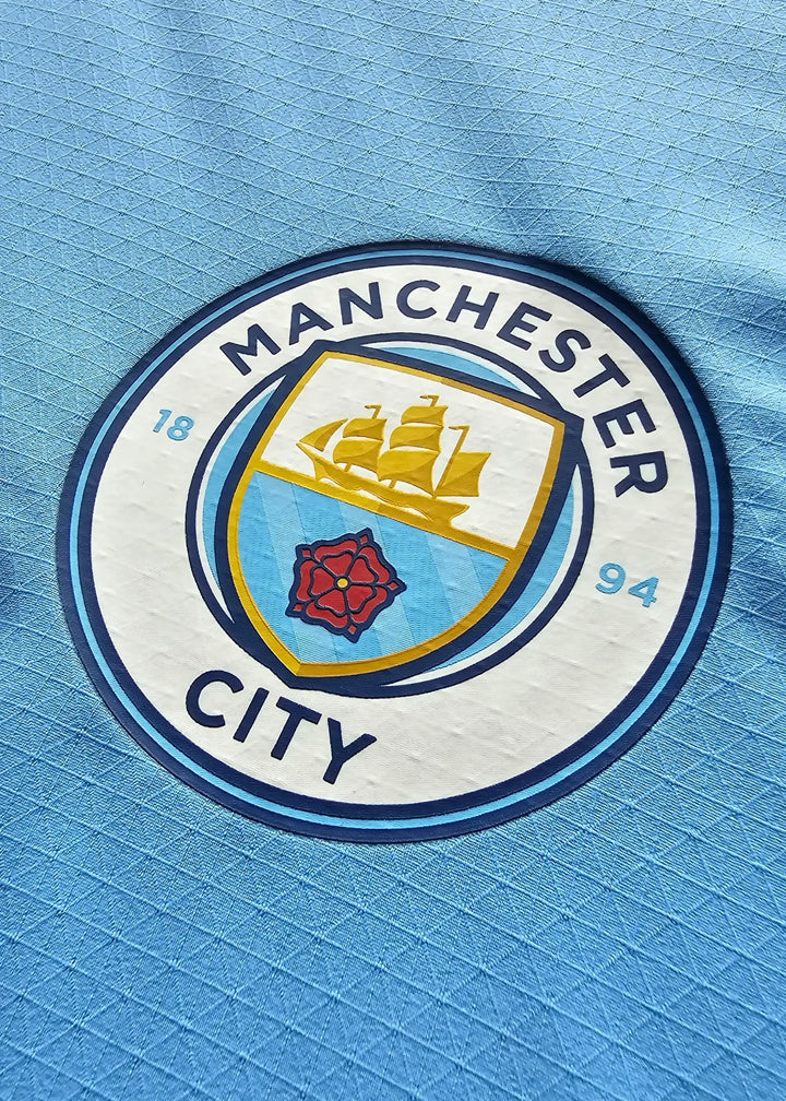 Manchester City crest featuring a ship and a red rose, with &