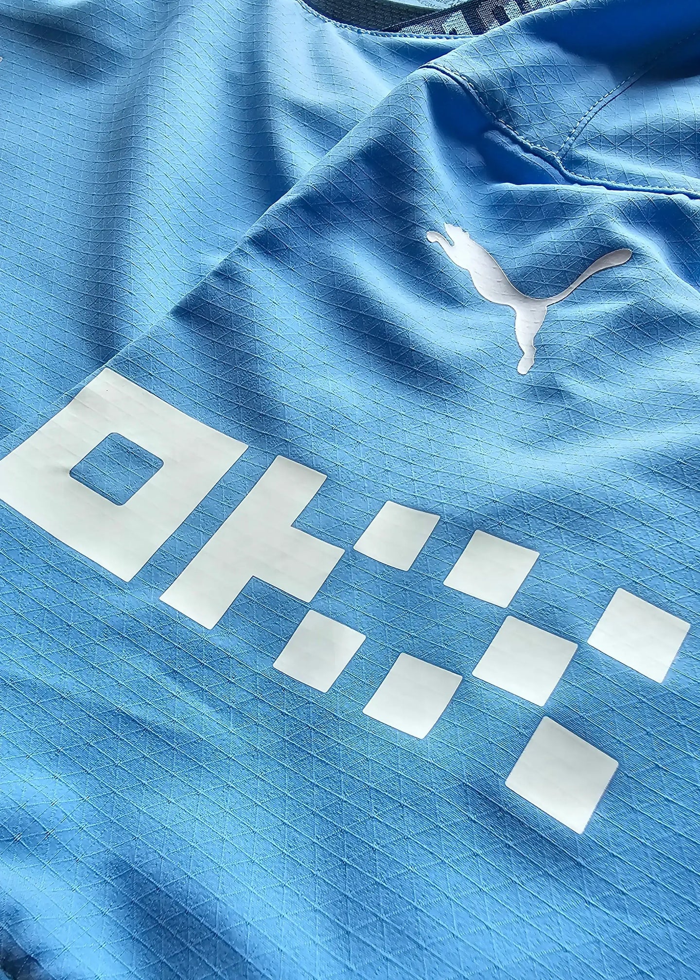 Detail view featuring the Puma logo and white sponsor text on a blue football shirt.