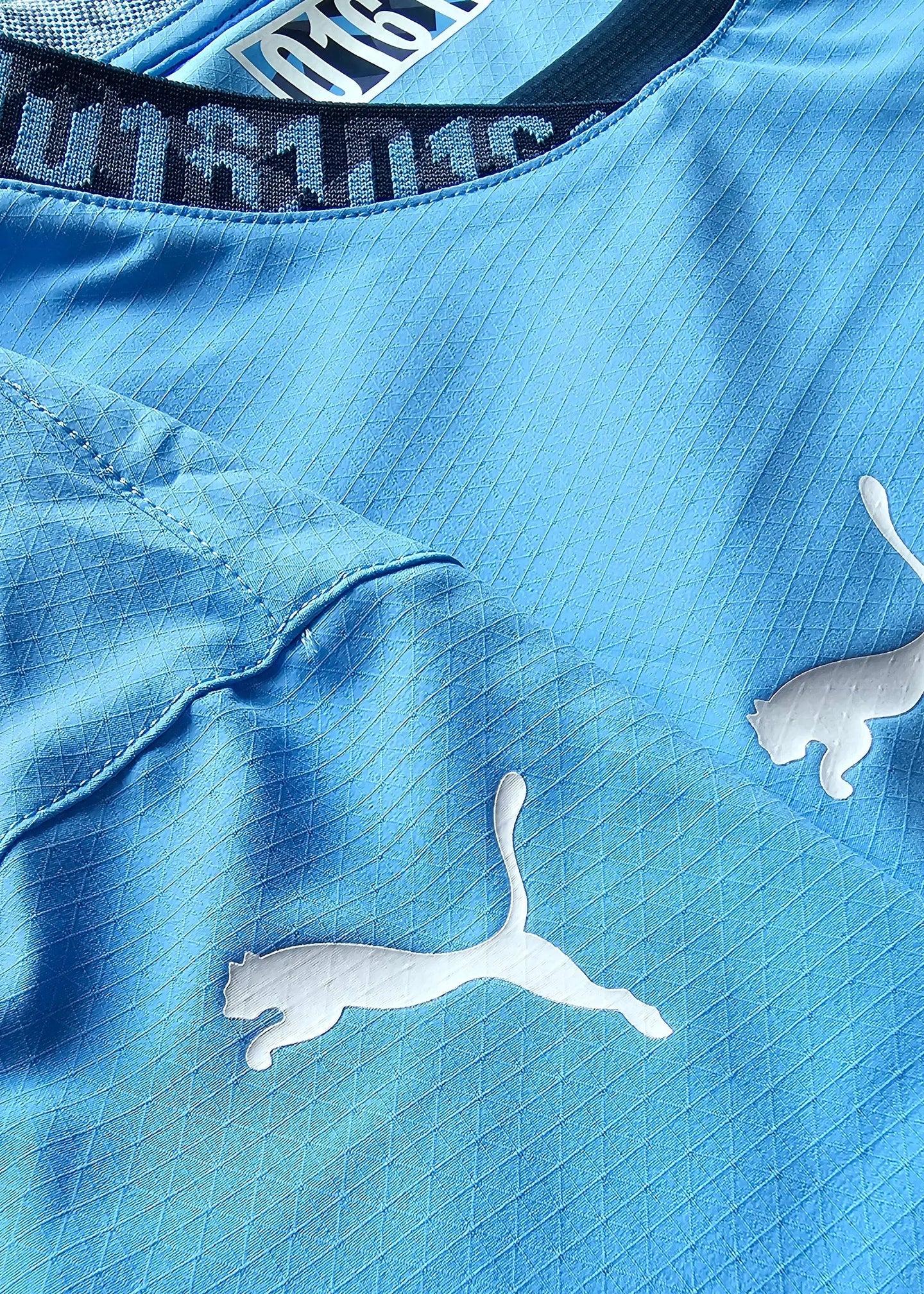 Close-up showing the blue fabric, Puma logo, and collar detail of the Manchester City football shirt.