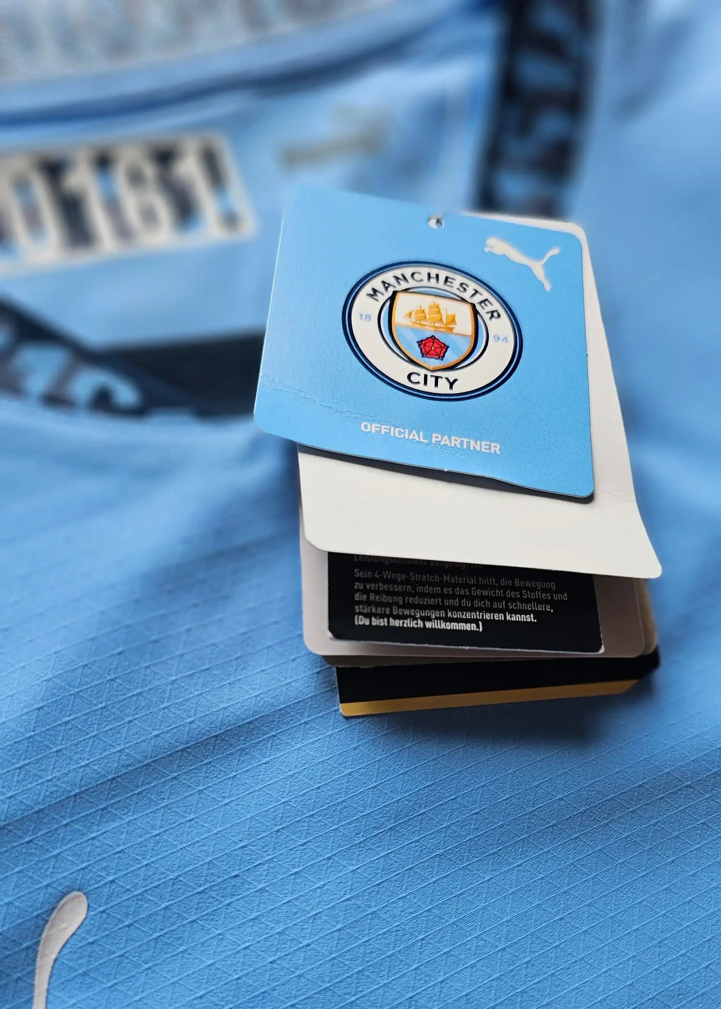 Detailed view of the Manchester City badge with 'OFFICIAL PARTNER' tag in blue, showing shirt texture.