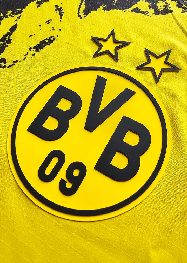 Crest detail showing black BVB lettering and two stars on a yellow football shirt.