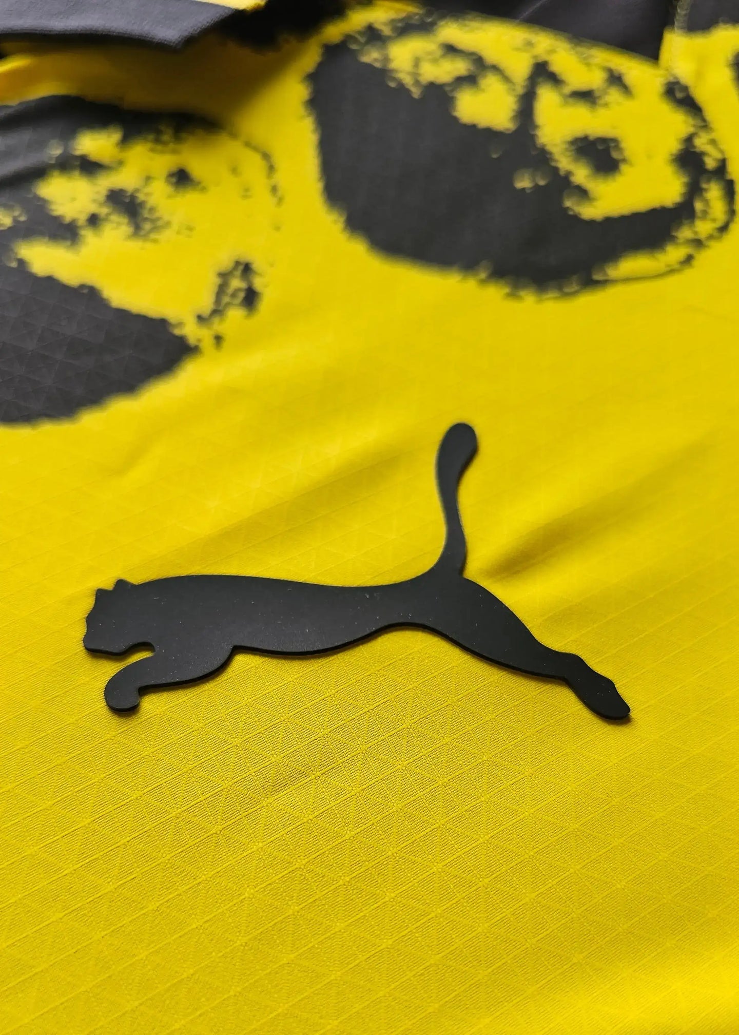 Close-up of the black Puma logo on a yellow football shirt.