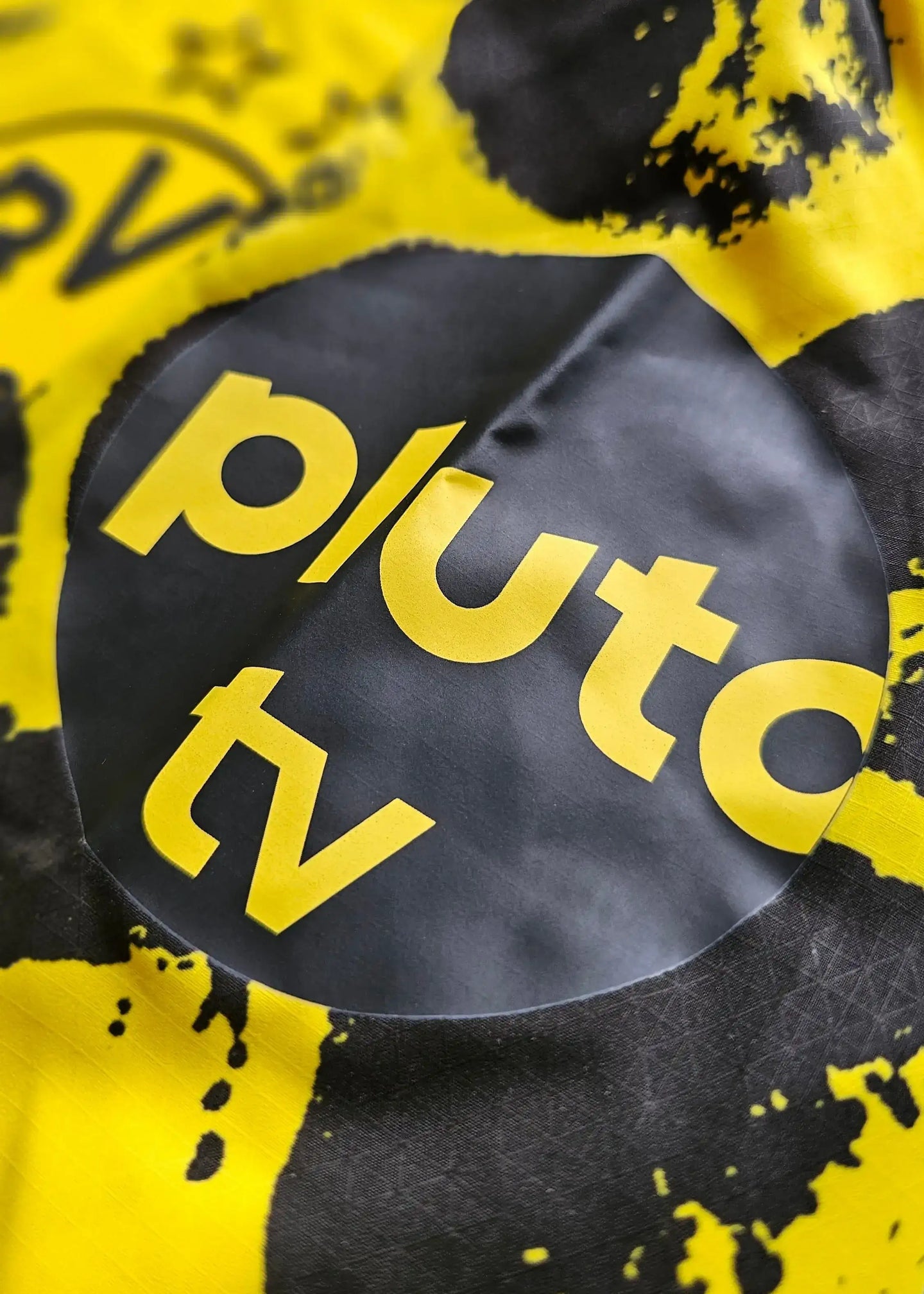Detail view of the Pluto TV sponsor logo in yellow and black on the football shirt.