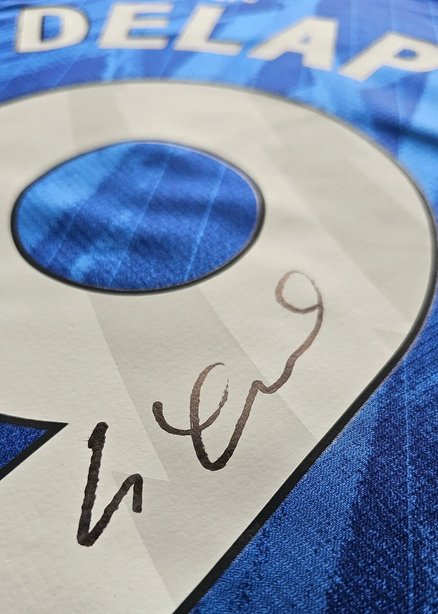 Close-up showing signature detail on No. 9 shirt featuring Delap and blue background.