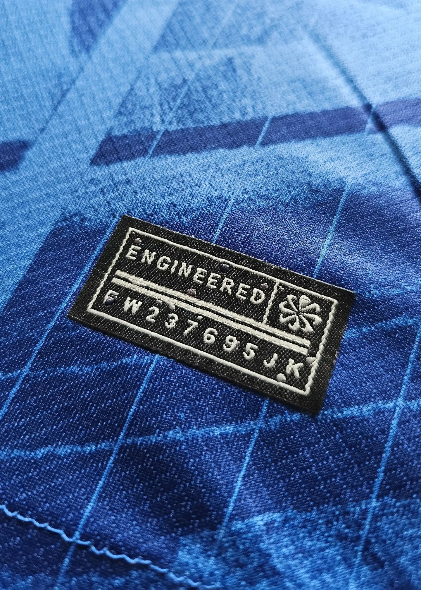 Close-up of engineered tag with text: ENGINEERED FW237695JK on a blue soccer jersey.