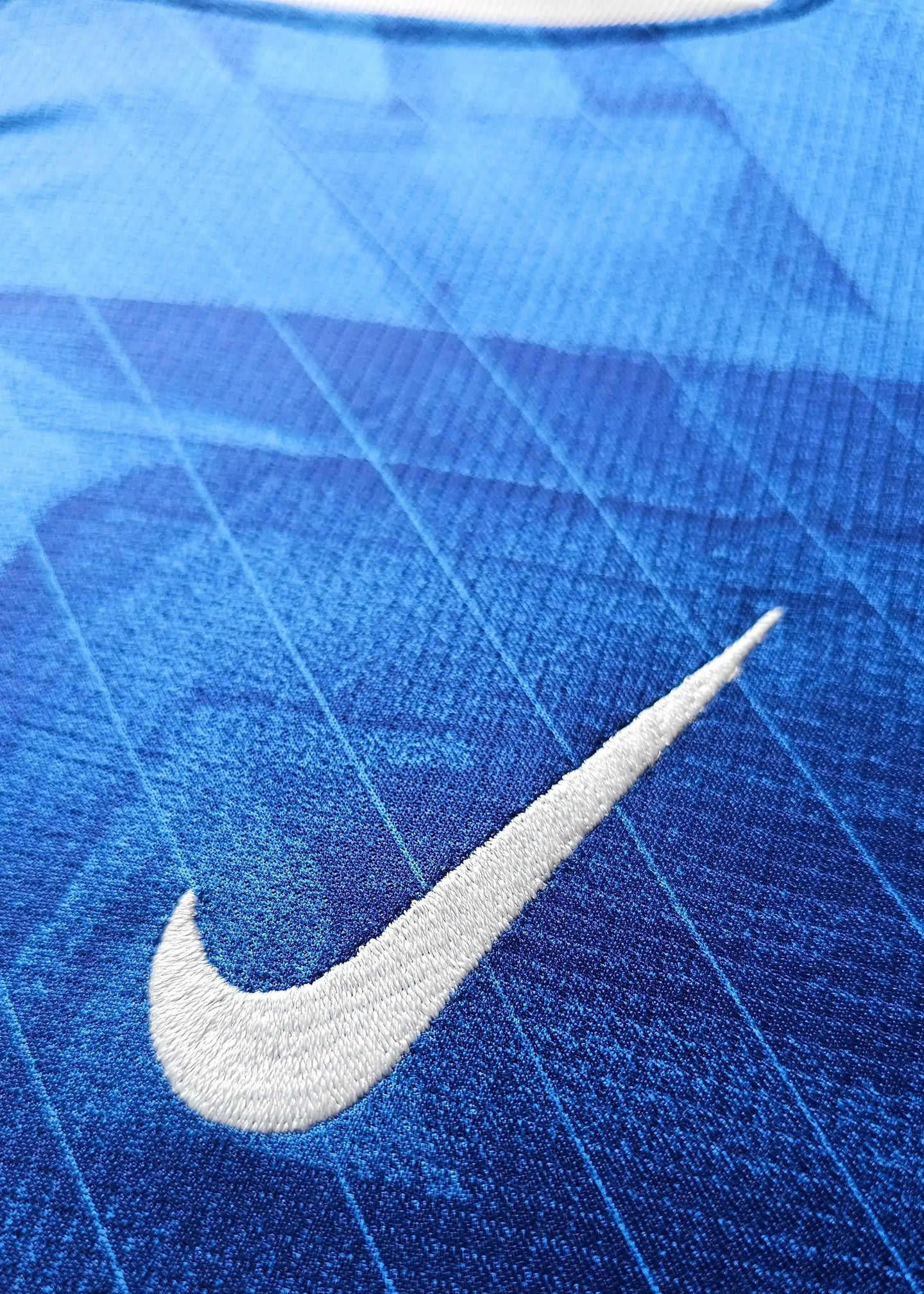 Close-up of blue fabric with prominent white Nike logo embroidered on the football shirt.