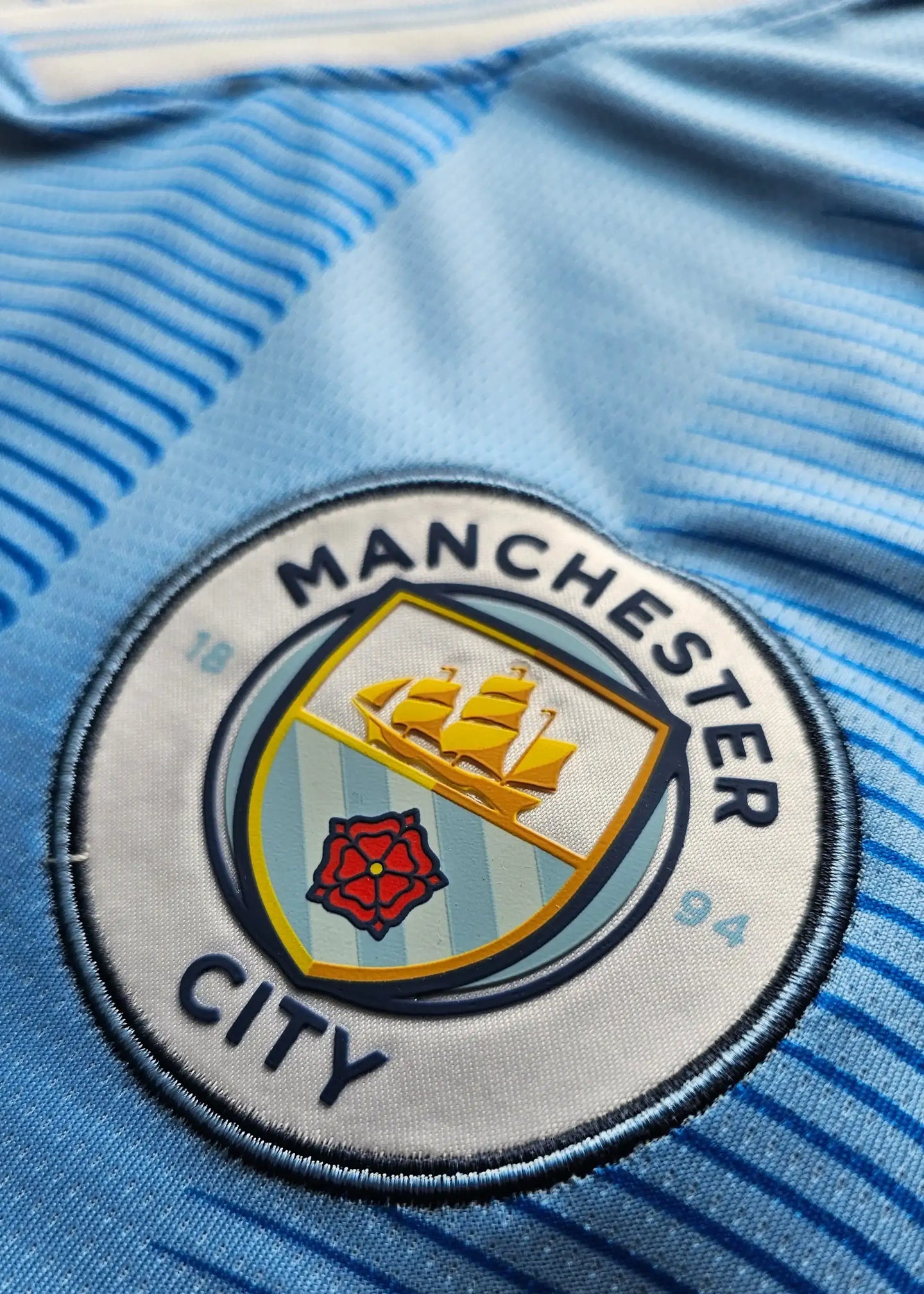 Crest detail showing Manchester City emblem with ship and red rose on a blue background.