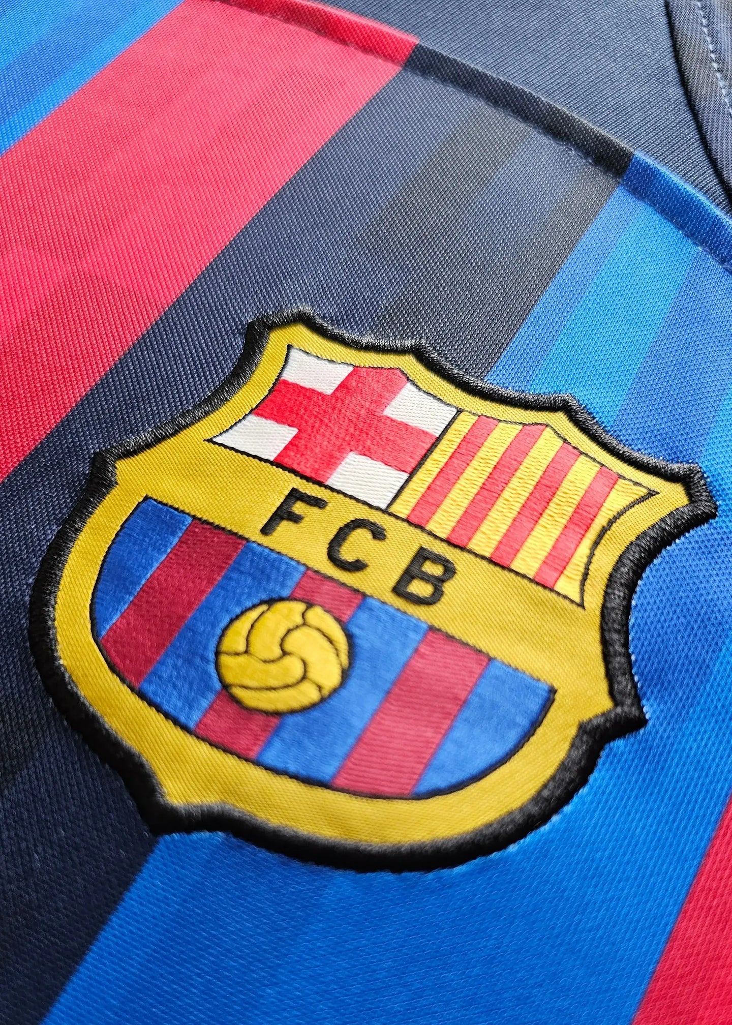Close-up of the FC Barcelona crest featuring red and blue stripes and the embroidered FCB logo.