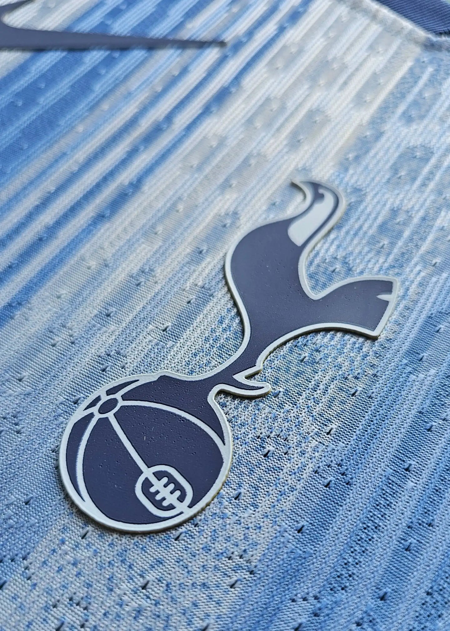 Close-up view of the Tottenham Hotspur crest on the signed football shirt in blue tones.