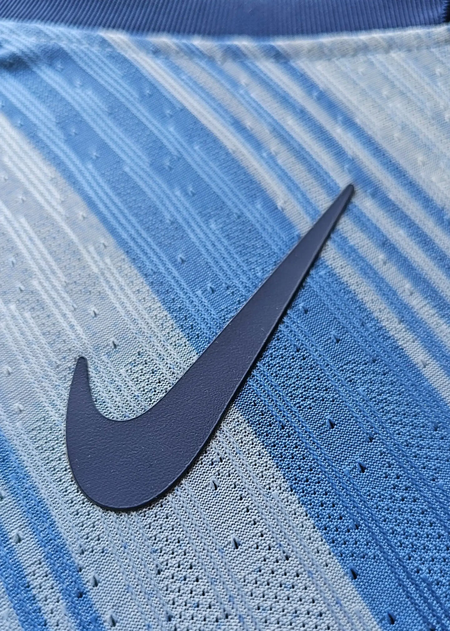 Close-up of Nike logo on a blue football shirt with a gradient design.