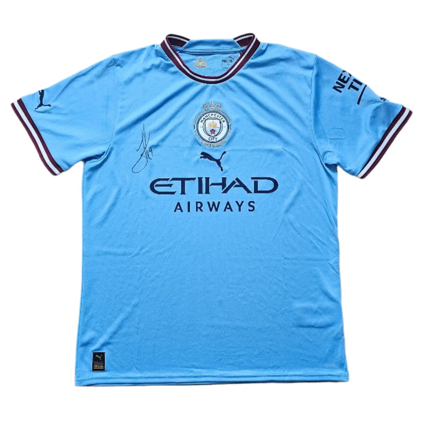 Front view of a blue Manchester City signed football shirt featuring the crest and a signature.
