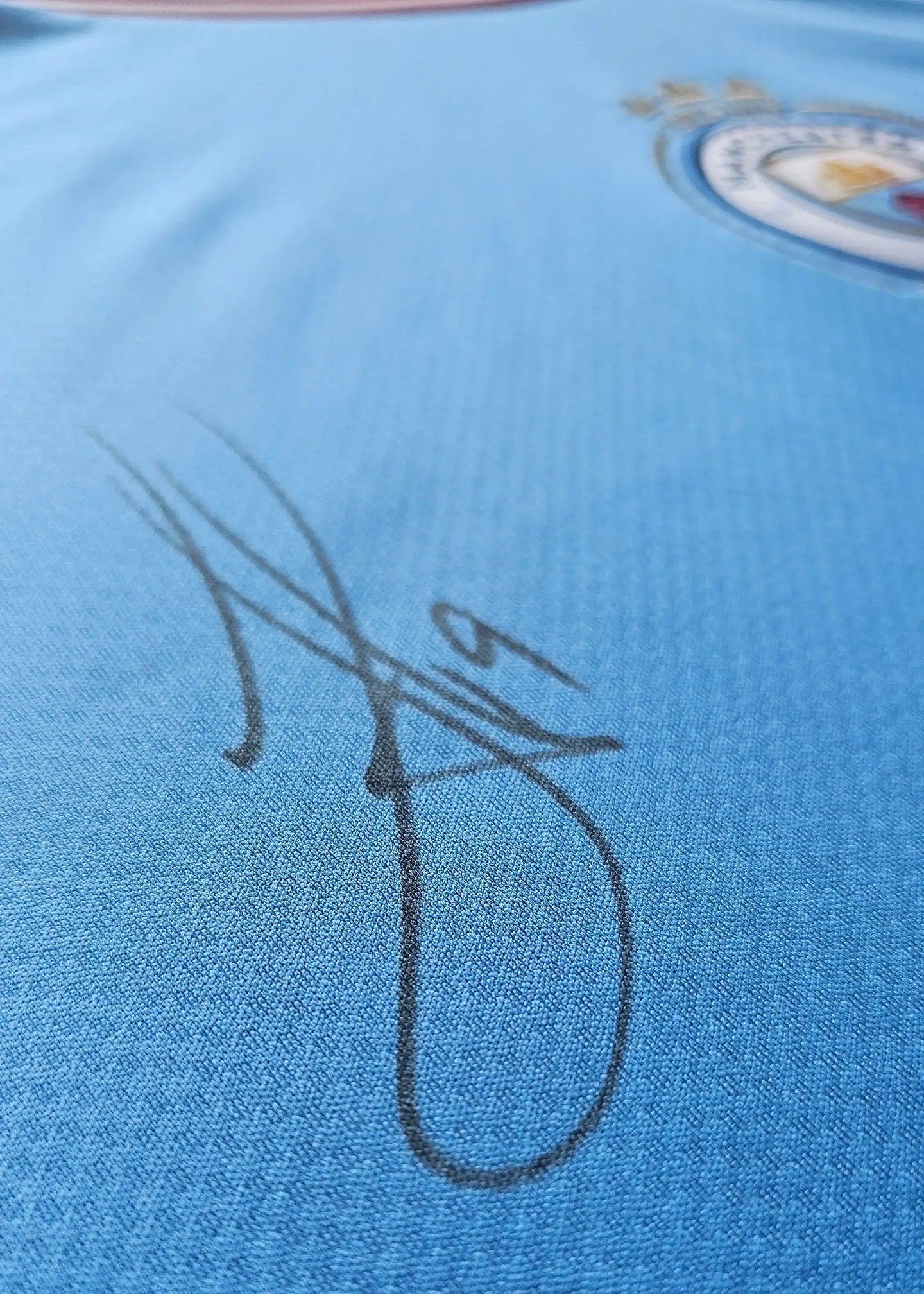Close-up of signature on blue football shirt with Manchester City crest visible.