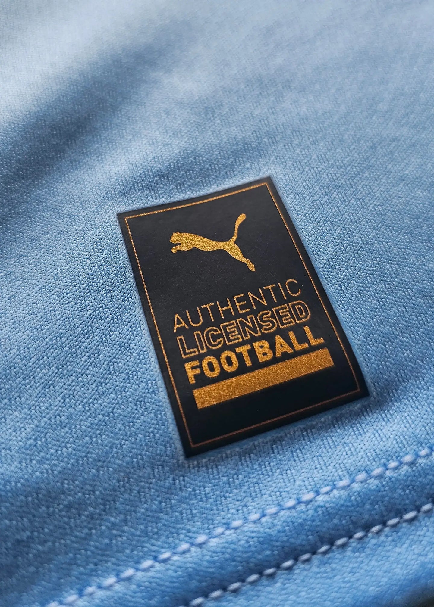 Close-up of the 'AUTHENTIC LICENSED FOOTBALL' label on a blue football shirt.