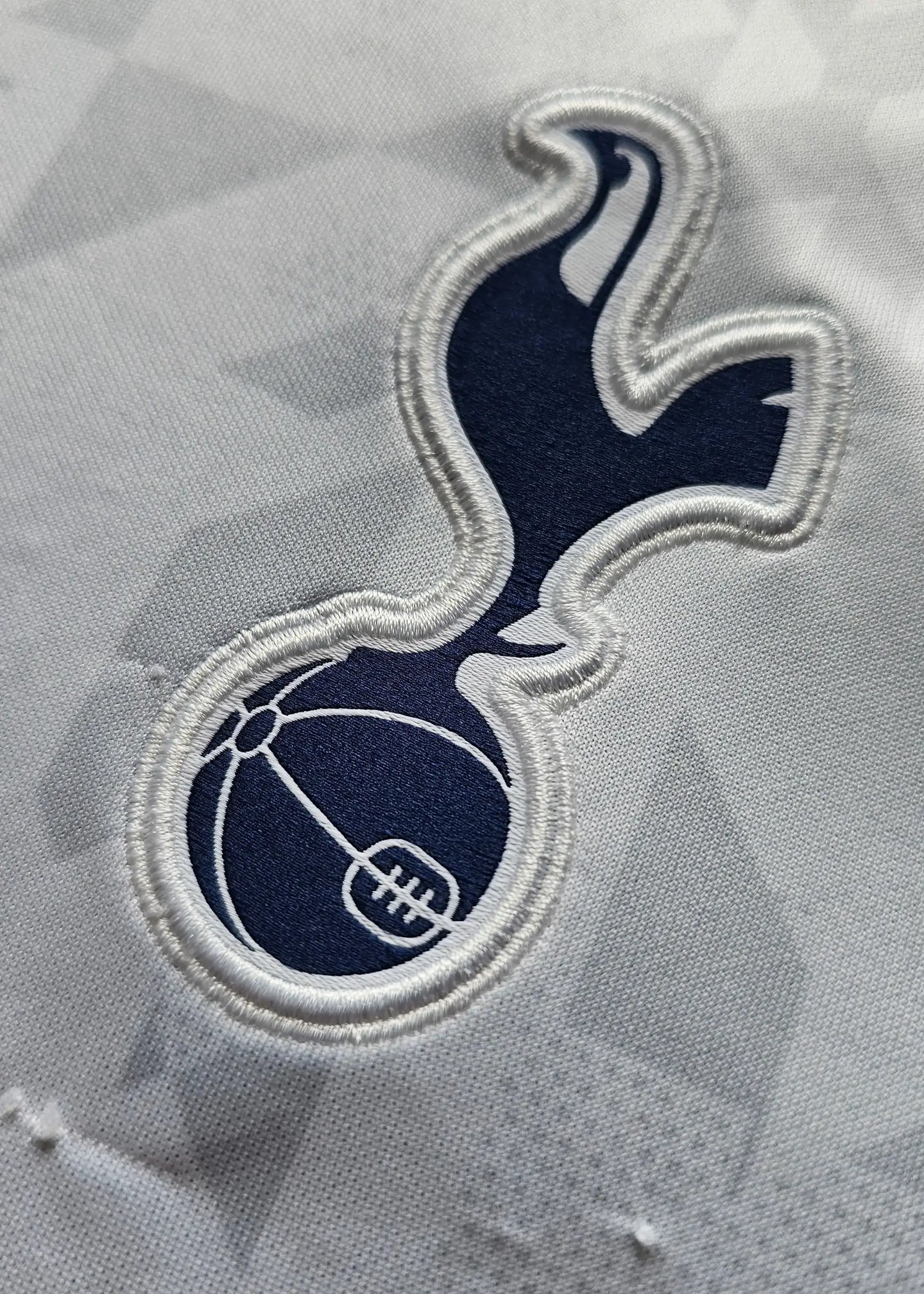 Close-up of the Tottenham Hotspur crest in navy on a white football shirt.