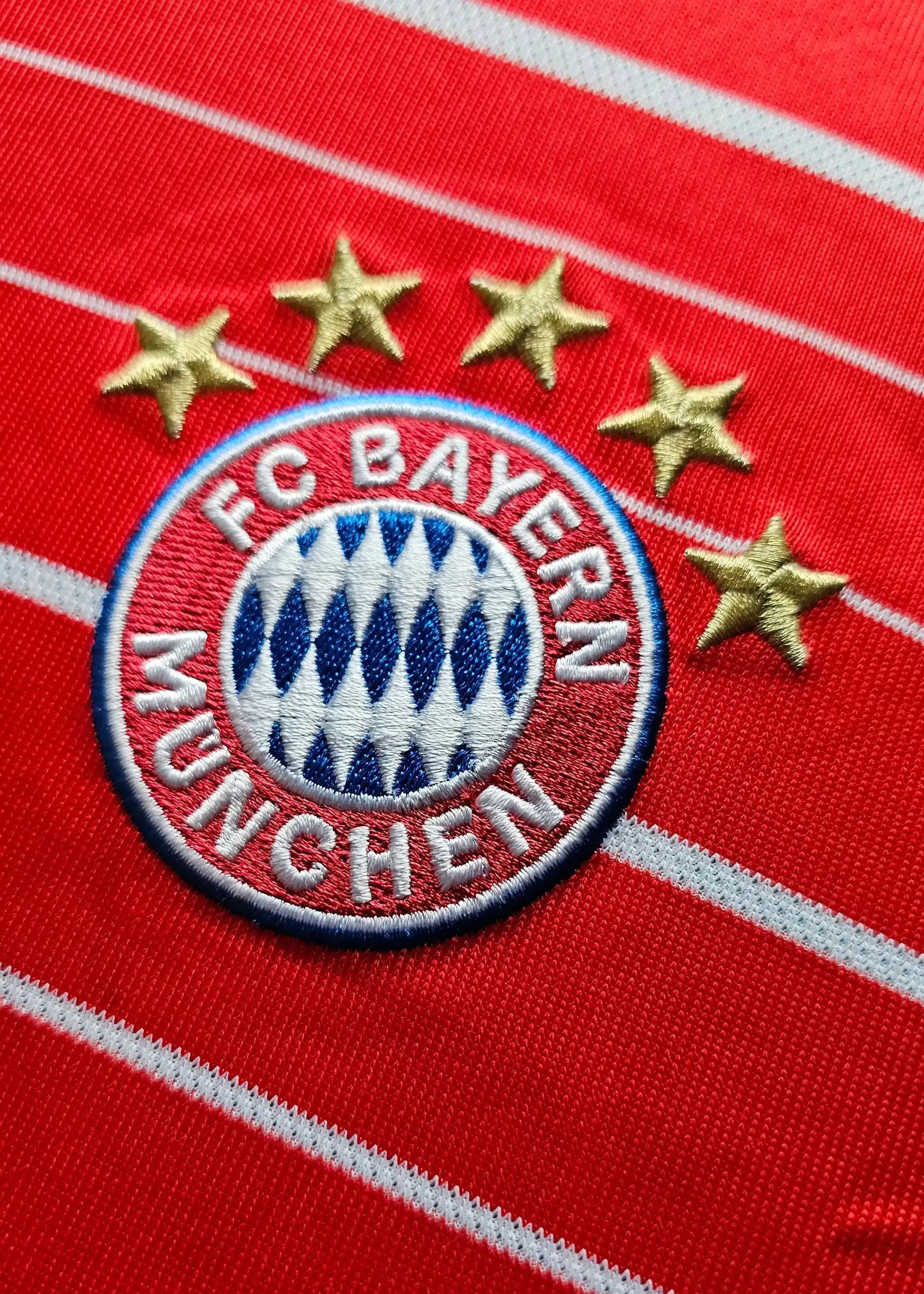 Detail of FC Bayern Munchen crest with five stars on a red football shirt.