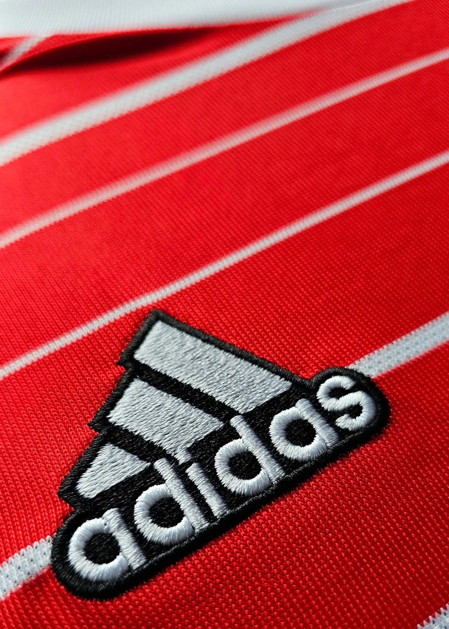 Close-up of the adidas logo on a red football shirt with white stripes.