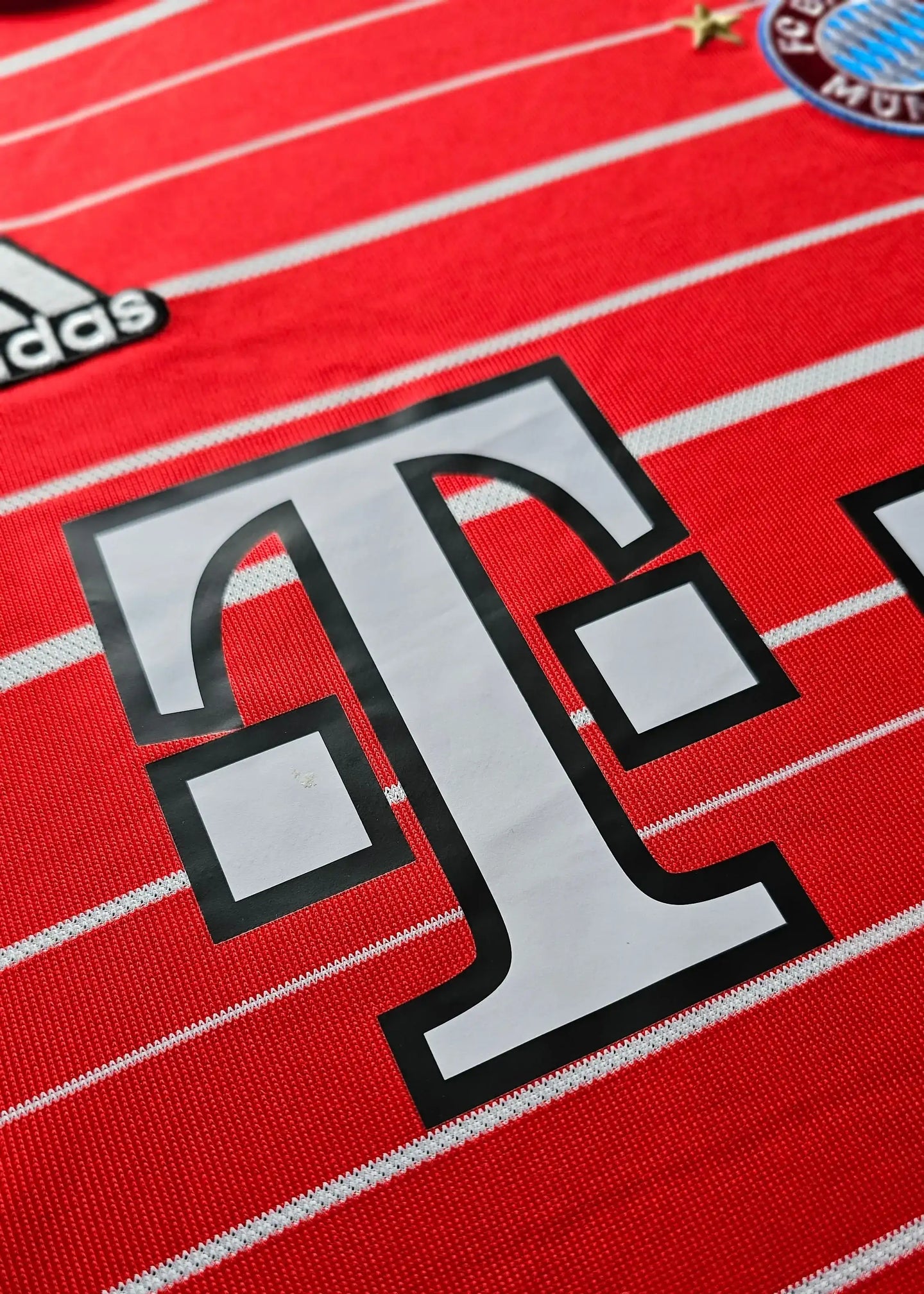Close-up showing the white Telekom logo on a red Bayern Munich football shirt with white stripes.