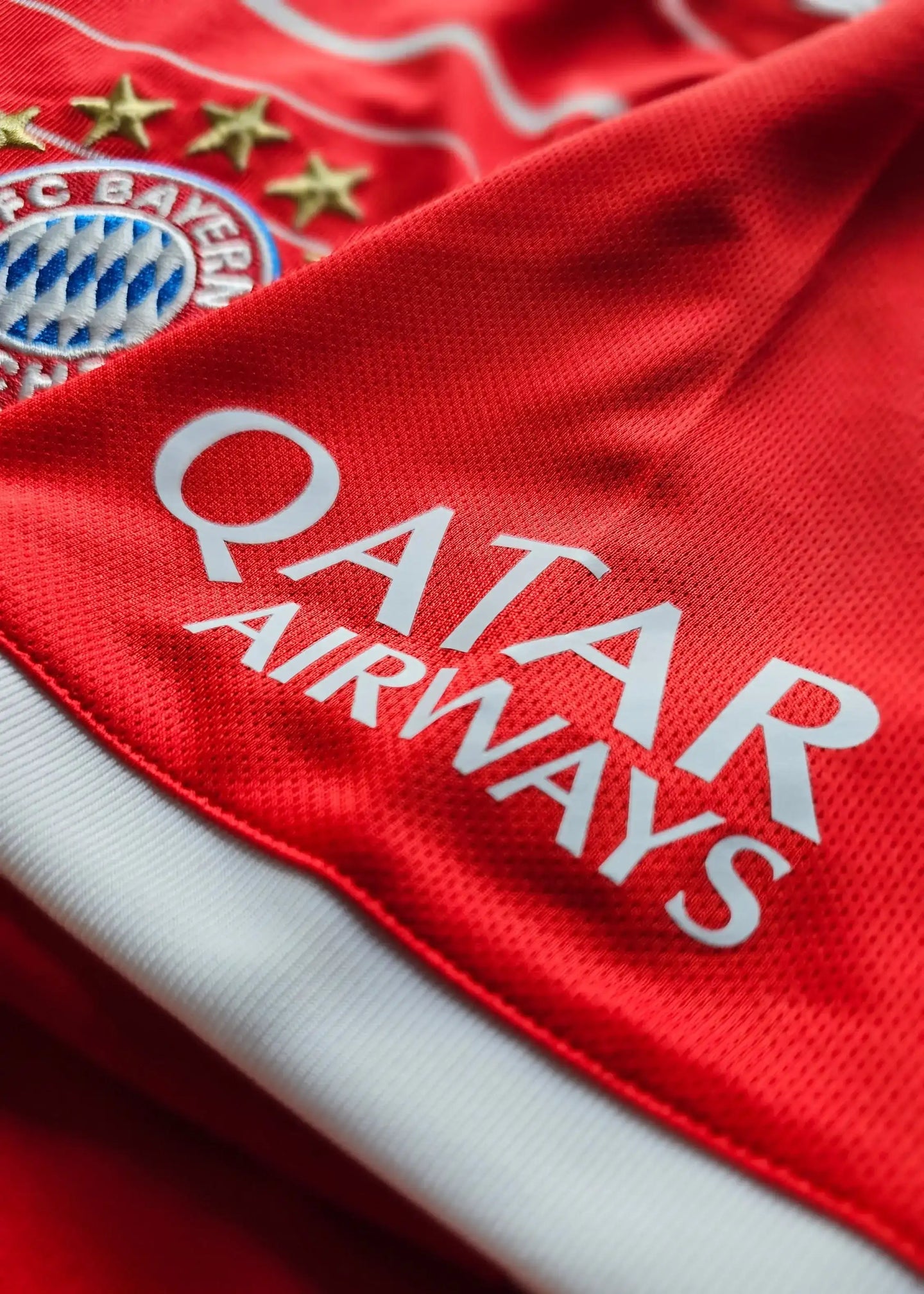 Crest of FC Bayern Munich with five stars and Qatar Airways sponsor text on red background.