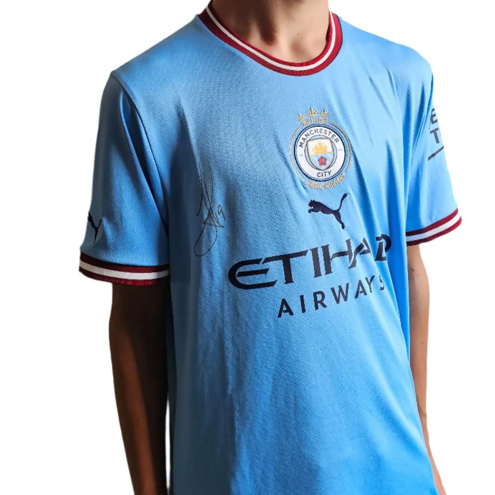 Front view of a light blue Manchester City signed football shirt with the crest and player signature.