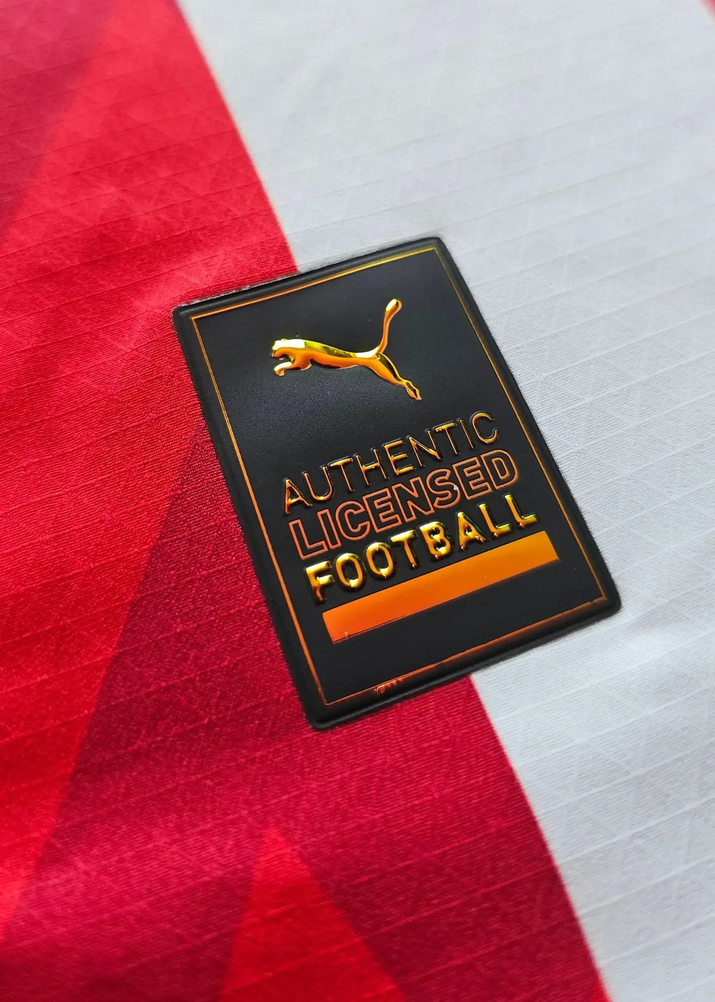 Close-up of the 'AUTHENTIC LICENSED FOOTBALL' label with a gold outline, on a red and white striped fabric.