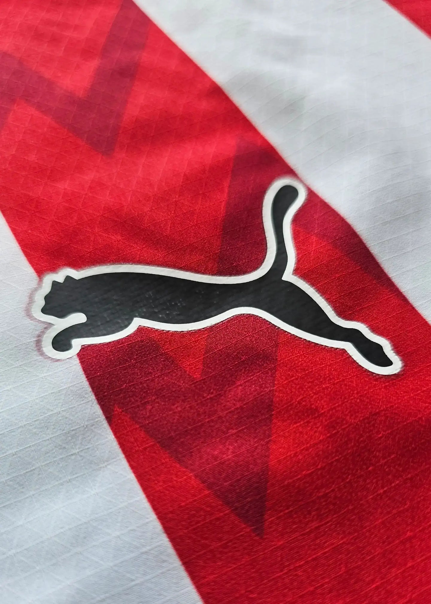 Close-up of PSV Eindhoven crest detail featuring the Puma logo on a red and white striped football shirt.