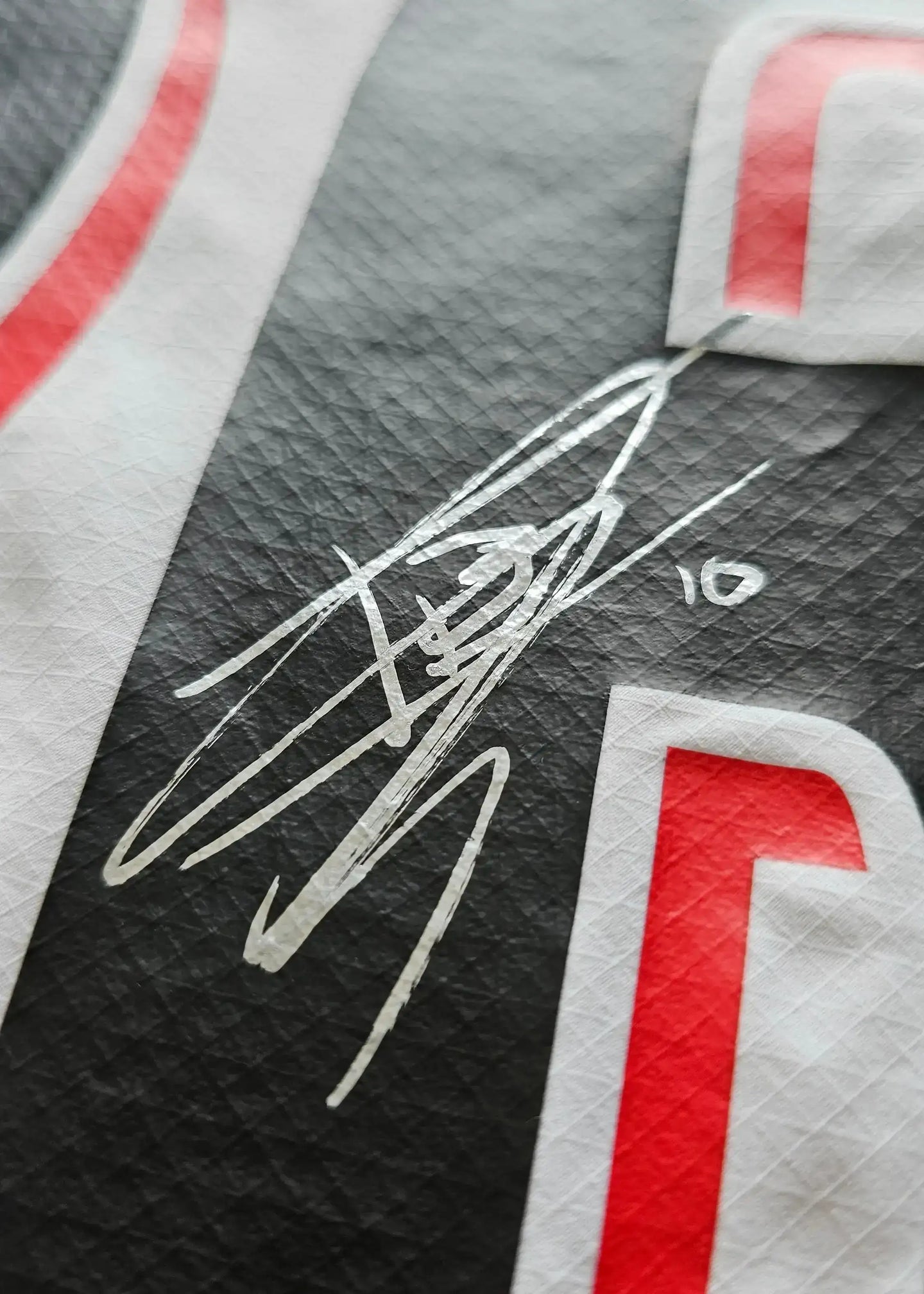 Close-up of Isaac Babadi's signature on the black and red PSV signed football shirt.