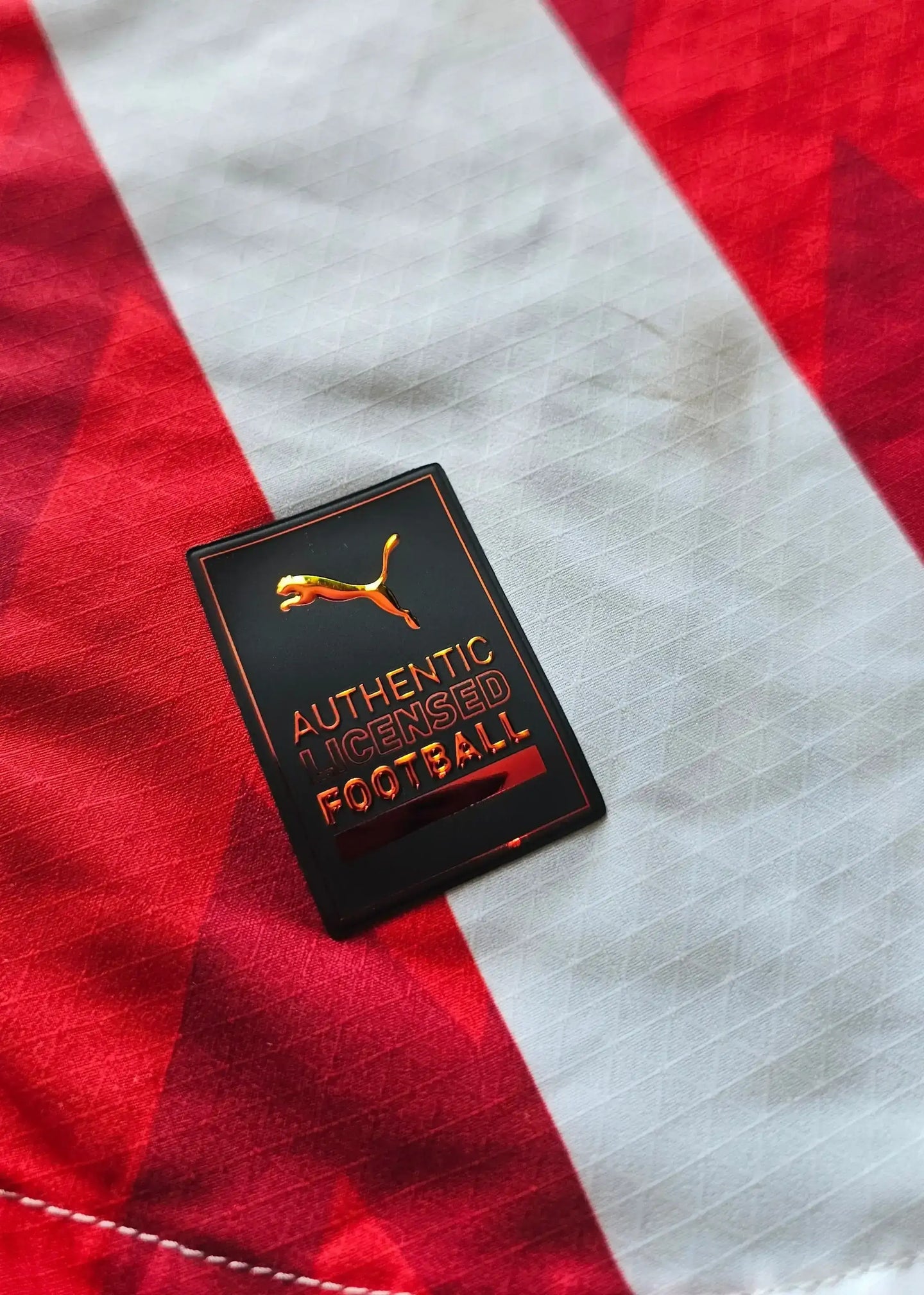 Puma badge with text 'AUTHENTIC LICENSED FOOTBALL' on red and white striped football shirt.