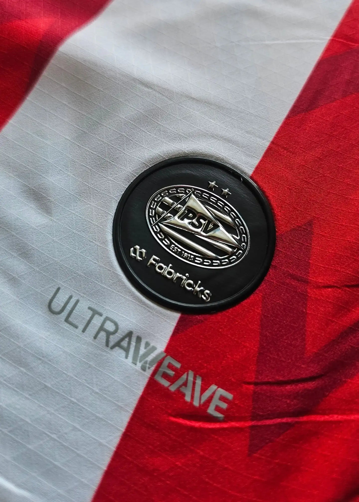 PSV crest with two stars above, and the text 'ULTRAWEAVE' and 'Fabricks' on a red and white striped shirt.
