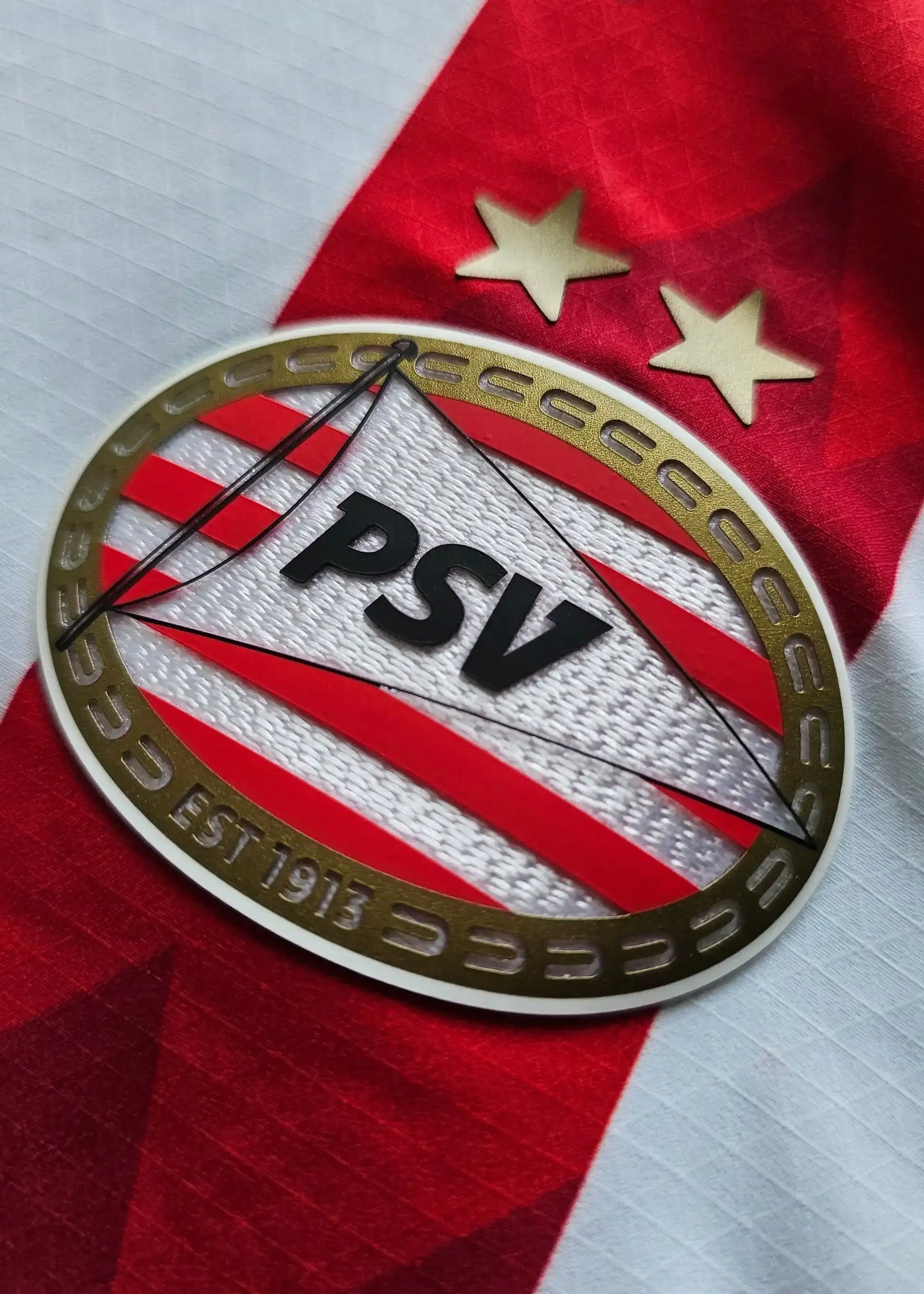 PSV crest with two stars and the letters PSV on a red and white striped football shirt.
