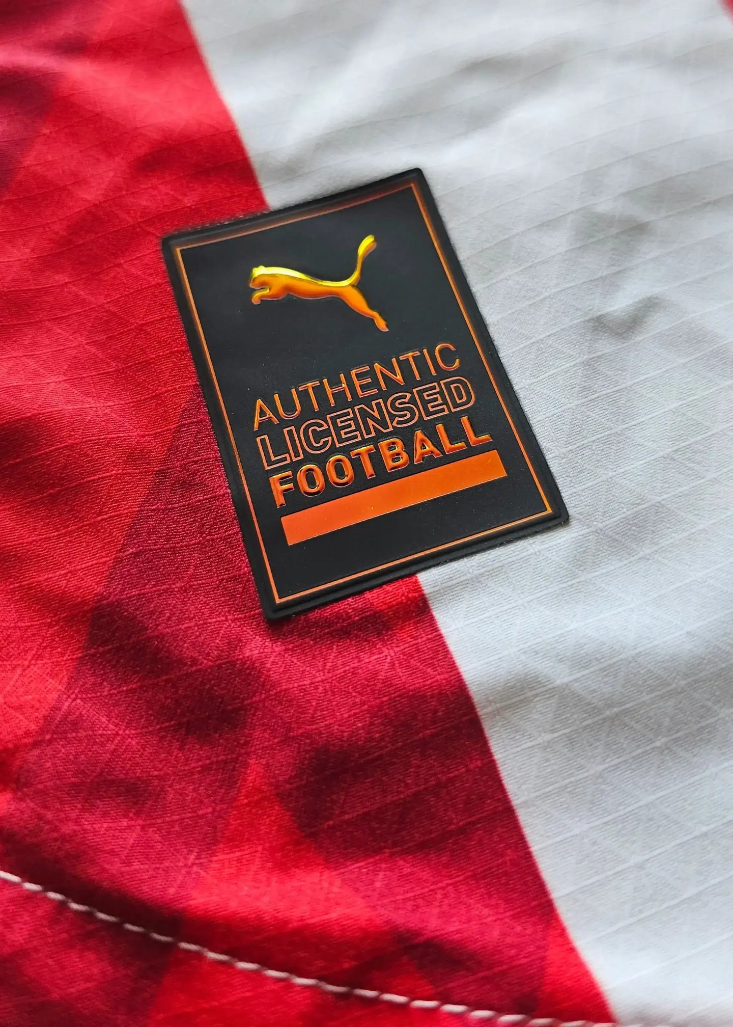 Puma label showing text 'AUTHENTIC LICENSED FOOTBALL' on red and white football shirt.