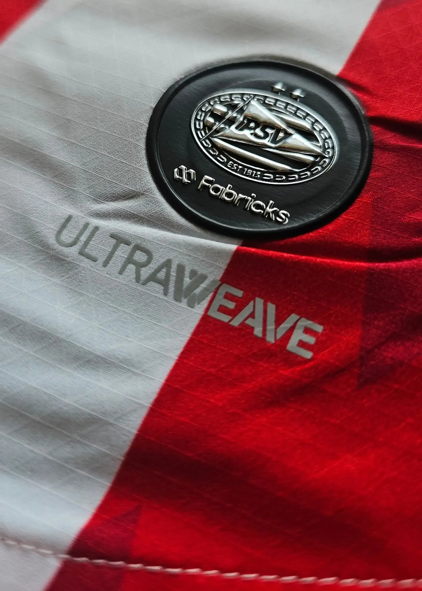 Close-up showing PSV badge and ULTRAWEAVE detailing on a red and white football shirt.