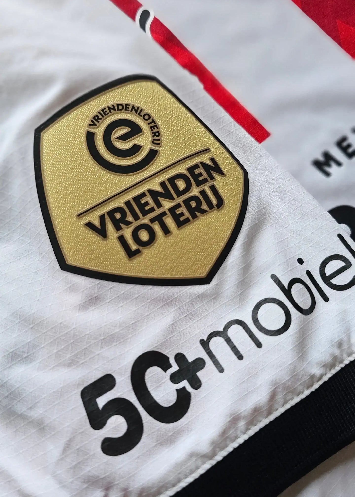 Close-up detail of the PSV Eindhoven crest featuring VRIENDEN LOTERIJ and 5C+mobiel logos.
