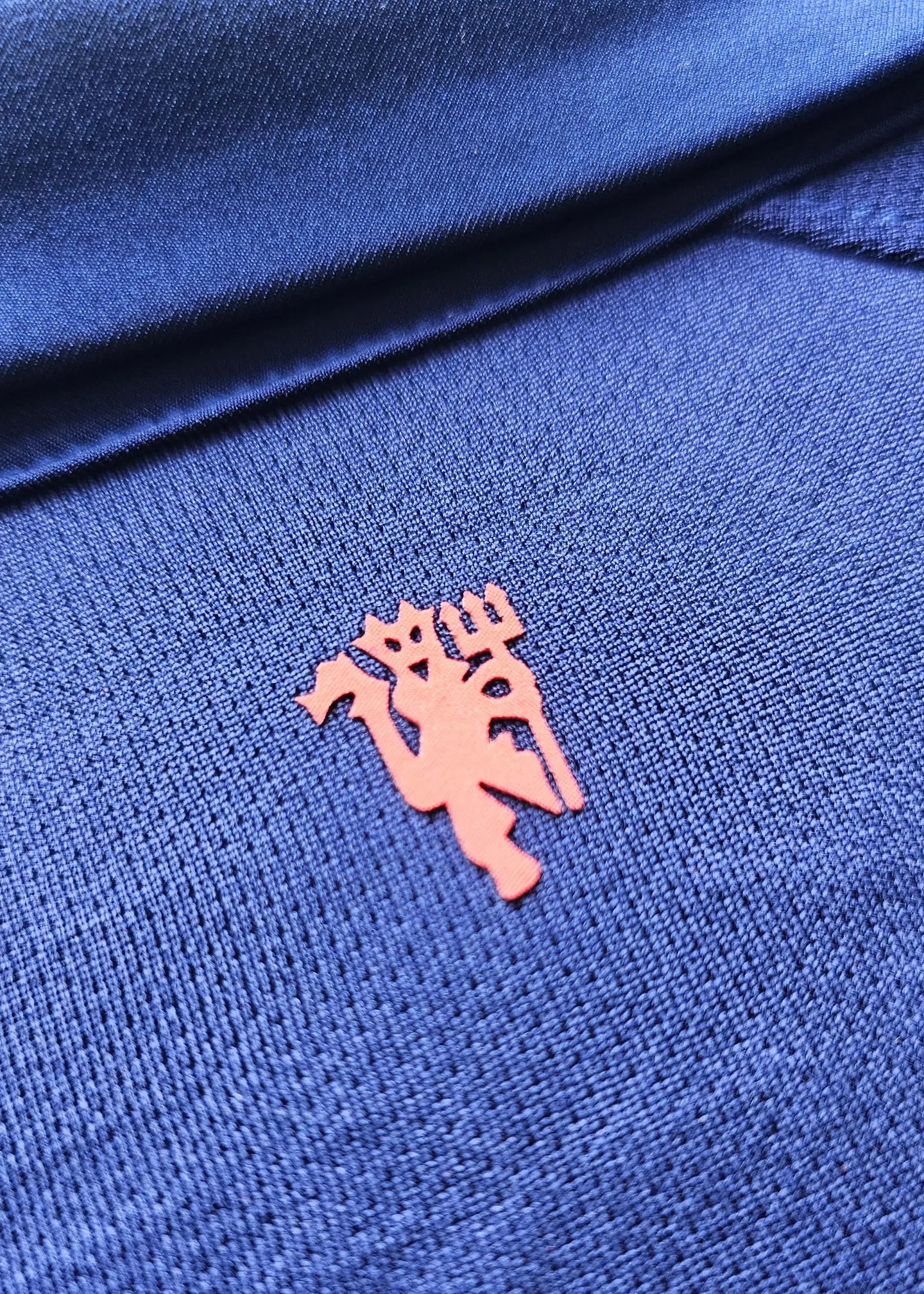 Close-up of the orange Manchester United crest on a blue football shirt.