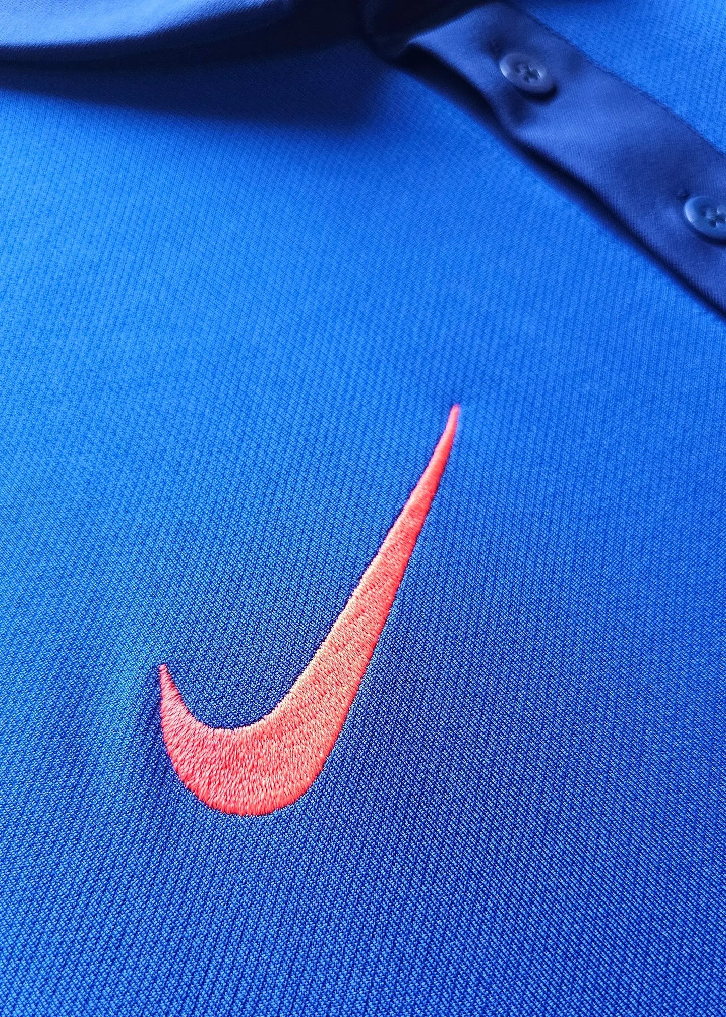 Close-up of the embroidered Nike logo in orange on a blue textured surface.