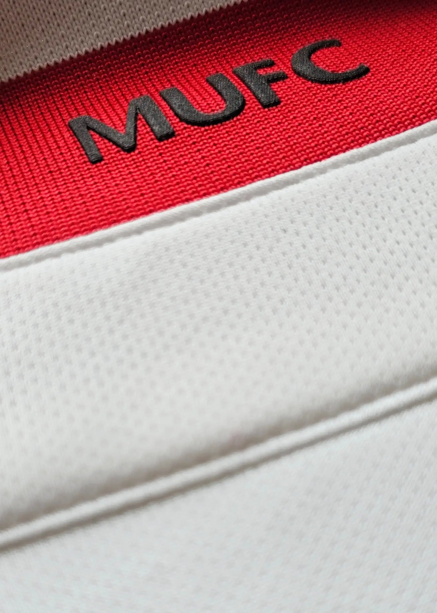 Close-up of the red tag displaying 'MUFC' stitched on the white fabric.