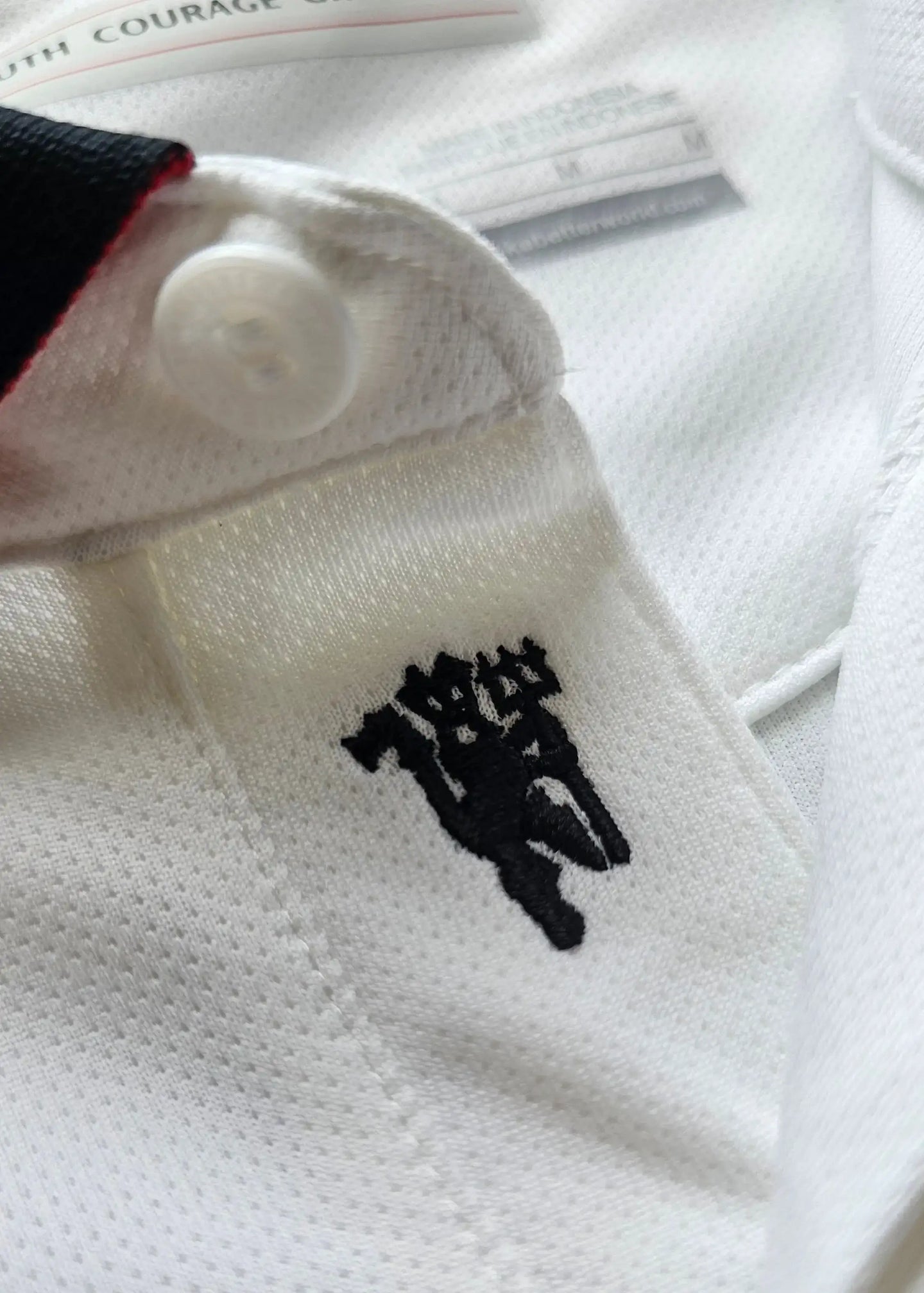 Detail of black player emblem on the collar of the white football shirt.