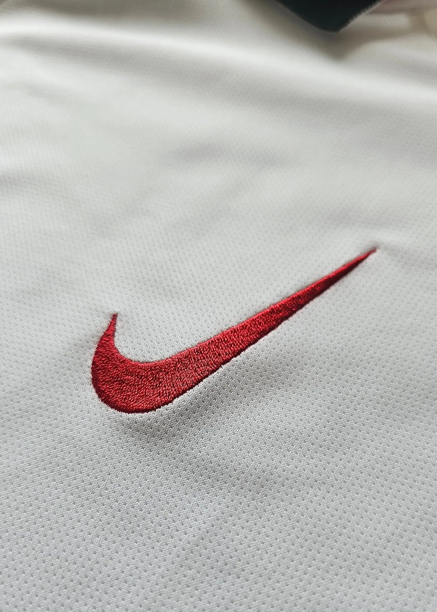 Close-up of the red embroidered Nike logo on a white football shirt.