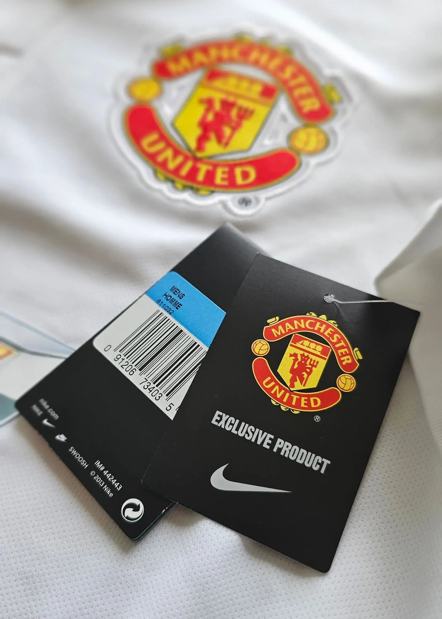 Close-up of Manchester United crest and product tags showing 'EXCLUSIVE PRODUCT' and barcode.