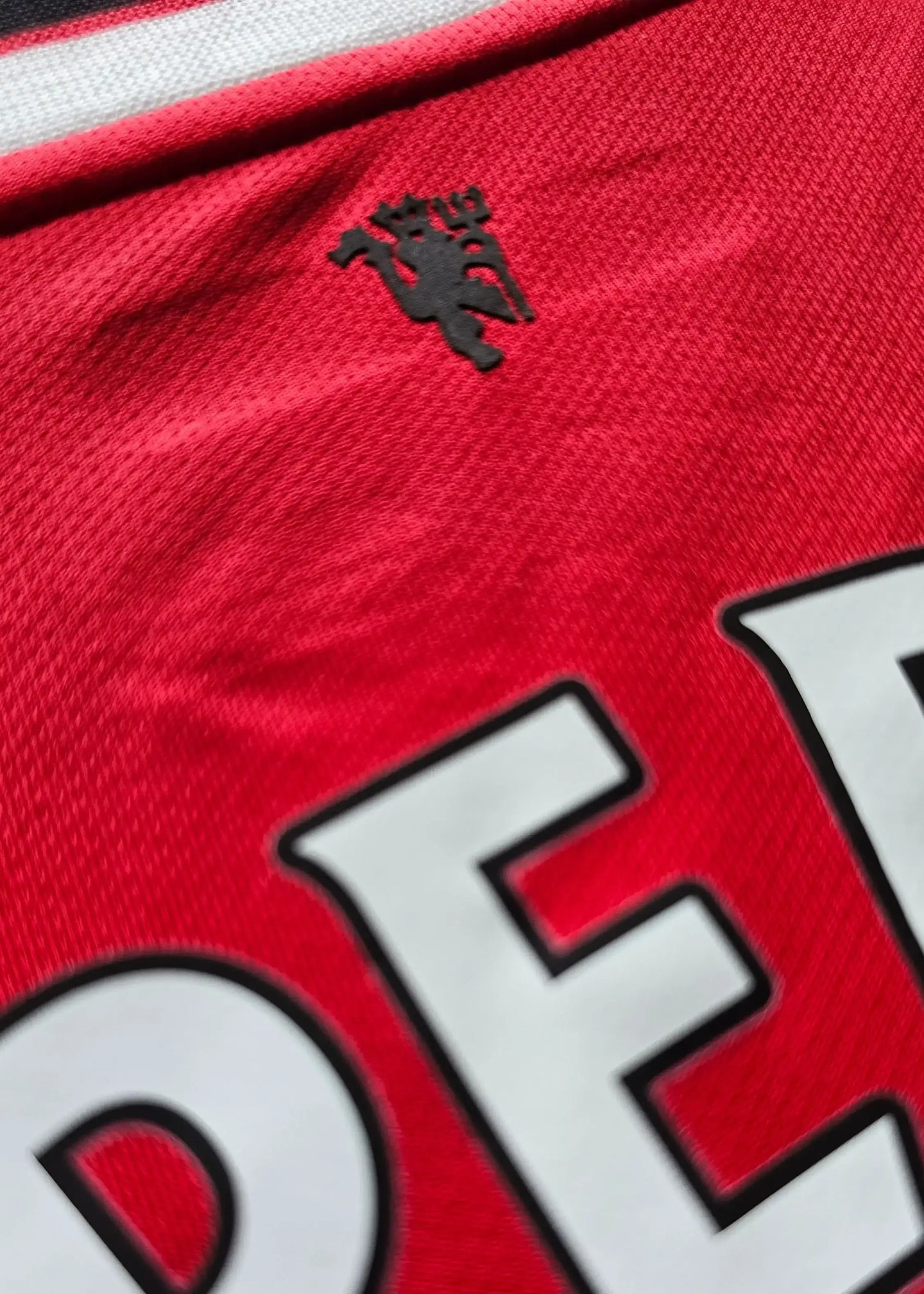 Close-up of Manchester United crest on the red shirt with black detailing.