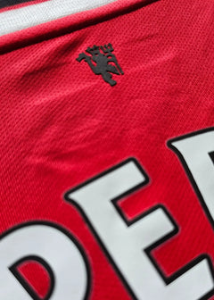 Close-up of Manchester United crest on the red shirt with black detailing.