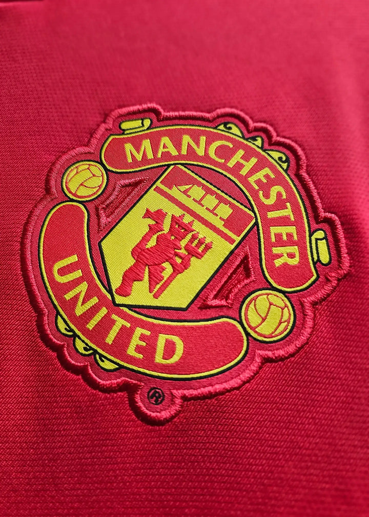 Manchester United crest embroidered in yellow on a red shirt.