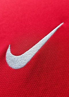 Close-up of the white Nike logo embroidered on a red shirt.