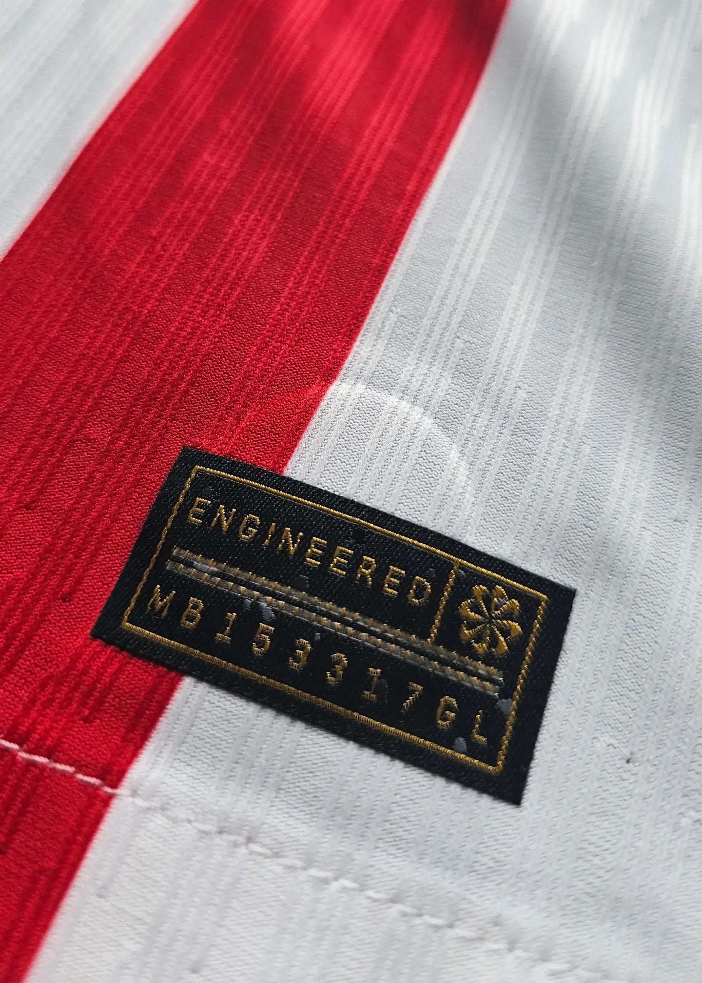 Label with the text 'ENGINEERED' and code 'MB153176L' on a red and white striped football shirt.