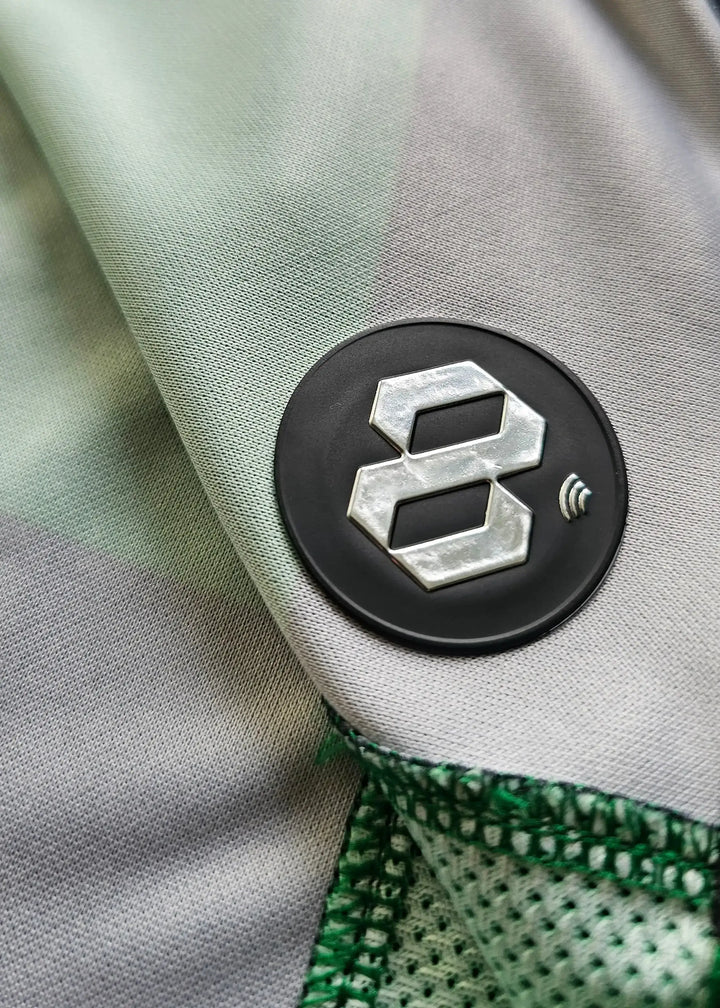Close-up of black circular badge with the number 8 on a striped green and grey shirt fabric.