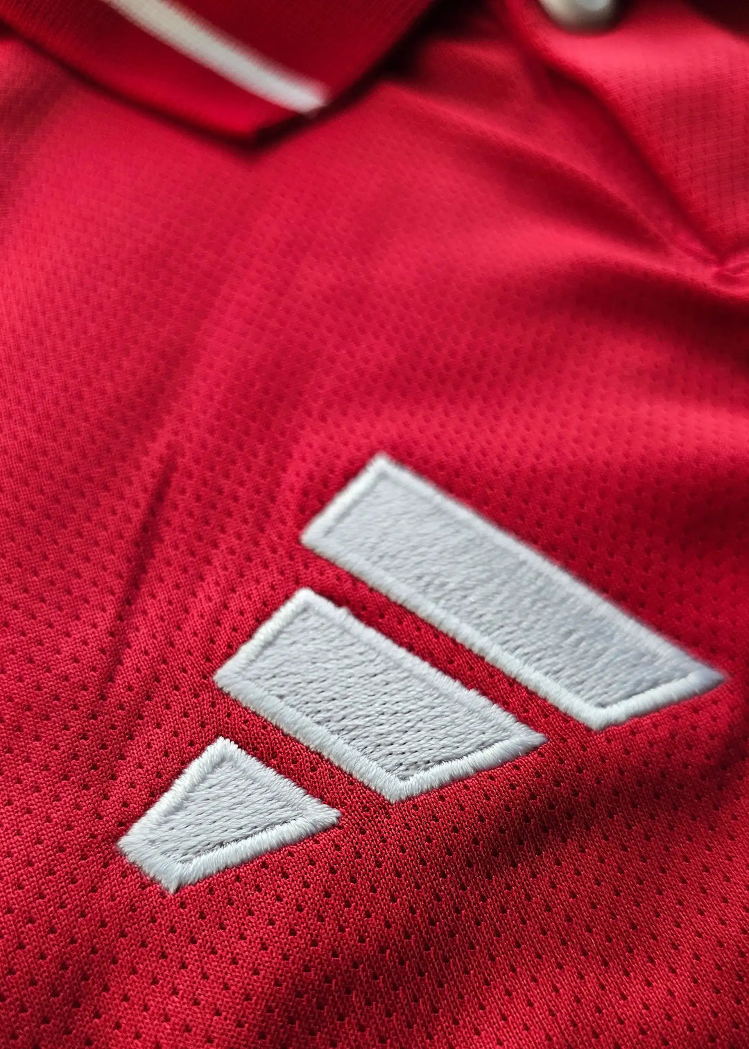 Close-up view of Adidas logo embroidered in white on a red football shirt.