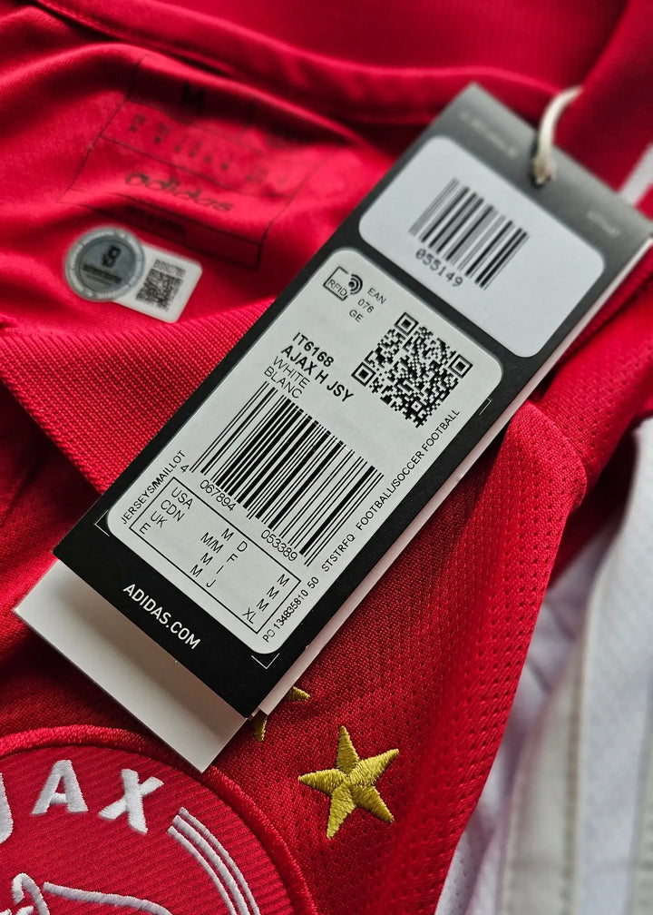 Detail view showing Ajax crest and size label on red football shirt with one star.