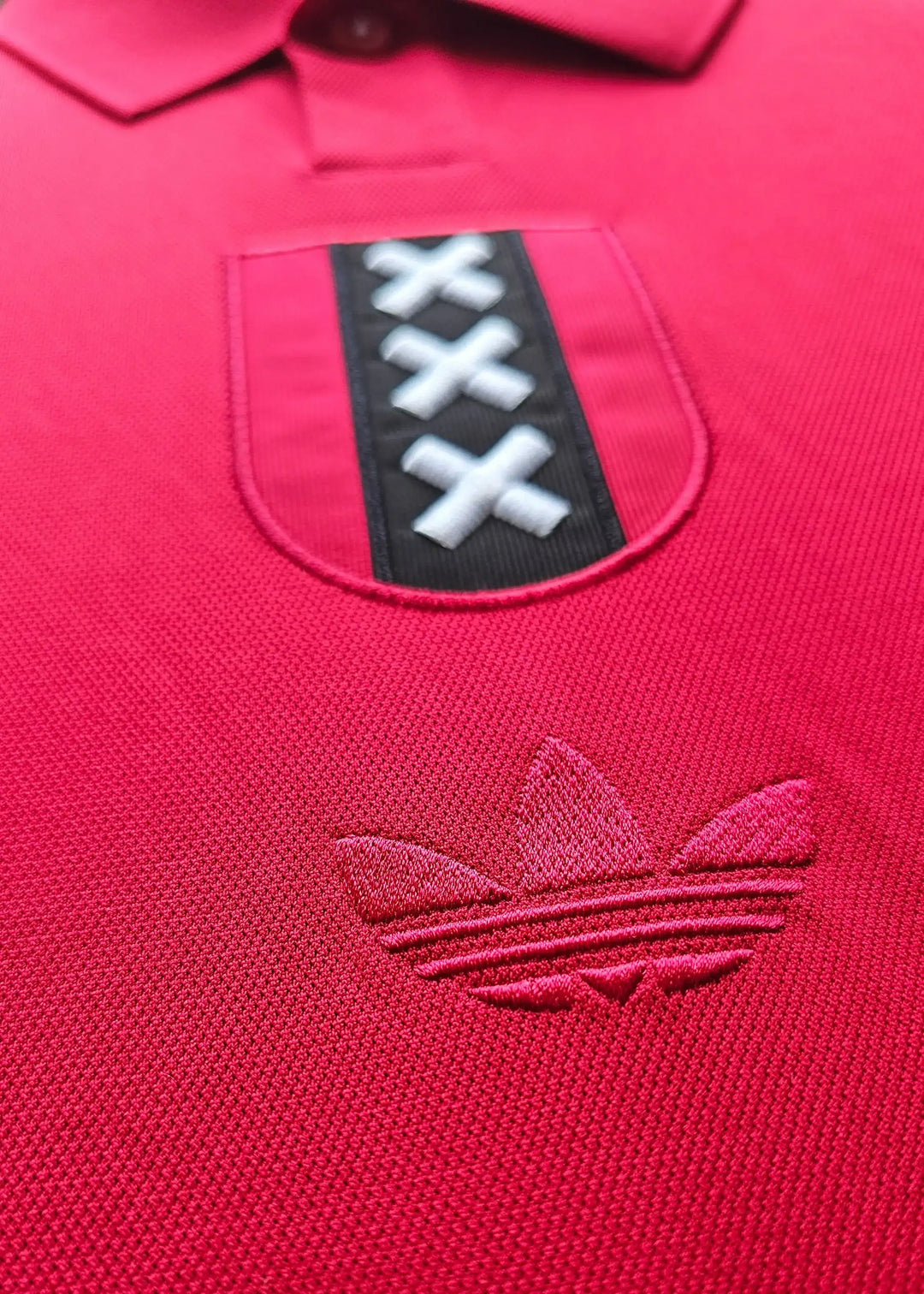Close-up view of Ajax crest featuring three X's on a red background and adidas logo.